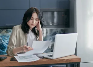 A concerned business owner reviewing financial paperwork and tax documents on a laptop regarding GST liabilities in Singapore.