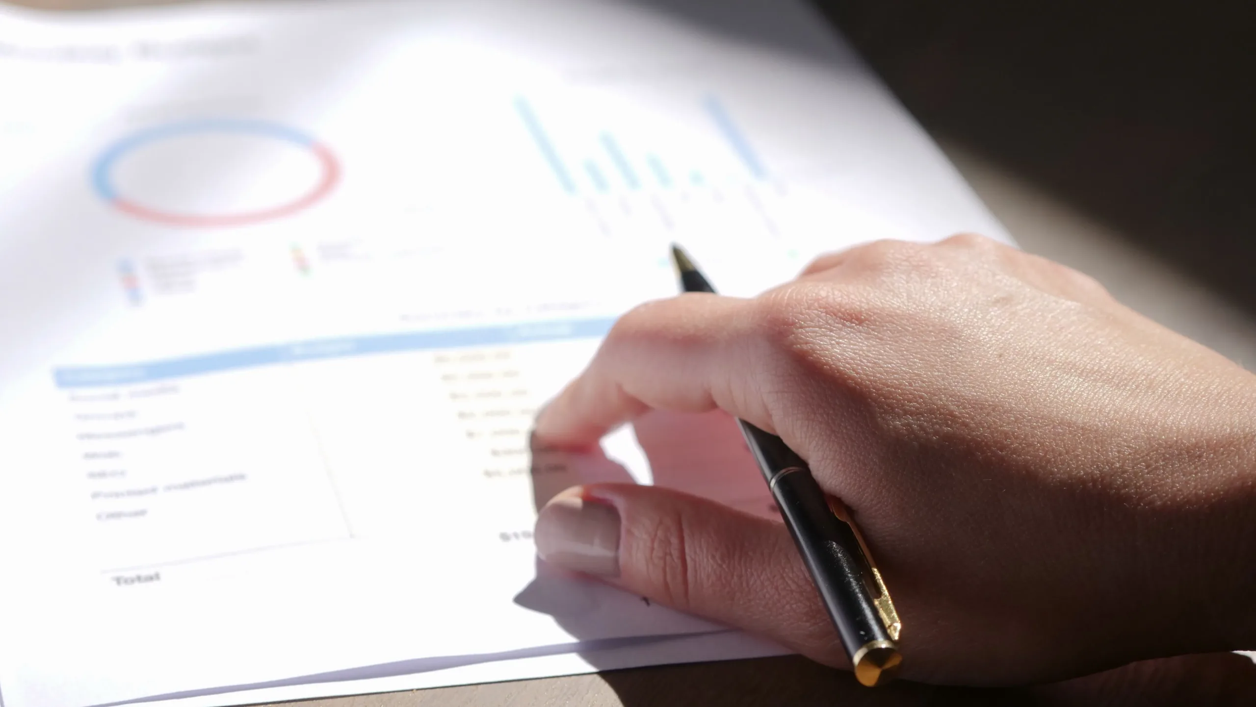 A person holding a pen while pointing at a printed financial report with charts and line items, evaluating proof of debt claims during a Singapore company liquidation.